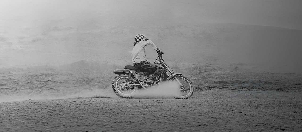 Pilote sur une moto tout-terrain vintage soulevant la poussière, photo noir et blanc